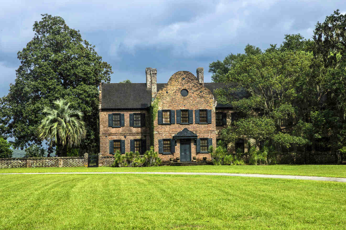 The historical Middleton Place House in Charleston, South Carolina, made of brick, with large windows, set against a lush landscape with towering trees and a manicured lawn